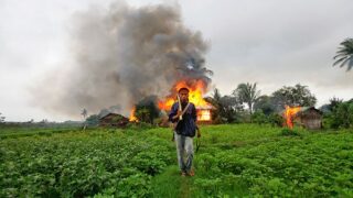 walks in front of burning houses during fighting